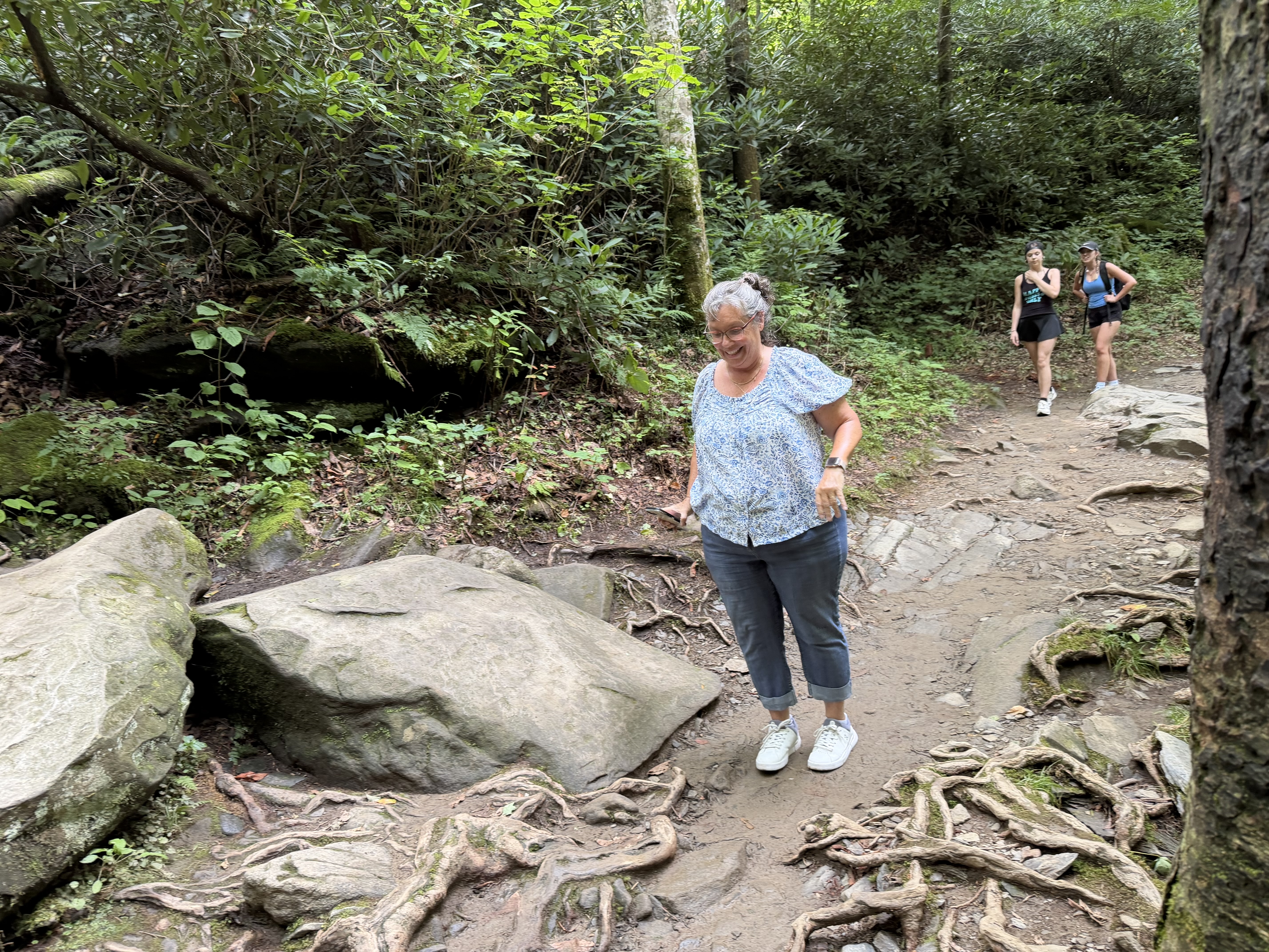 Colleen stepping down a root-covered, rocky section of the Rainbow Falls Trail in Great Smoky Mountains National Park, rhododendron crowding the trail on both sides